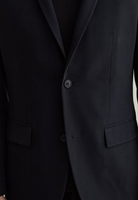 Blazer blu navale con due bottoni, reverse a scaldino e tessuto texturizzato. Presenta tasche laterali e una vestibilità sartoriale, che migliora la silhouette strutturata.