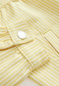 Tissu à rayures jaunes avec des lignes blanches, comportant un bouton et une poche. La texture semble douce et légèrement côtelée.