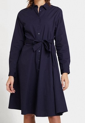 Vestido camisa azul marino de manga larga con botones en la parte delantera y cinturón anudado en la cintura, llevado por una persona contra un fondo liso.