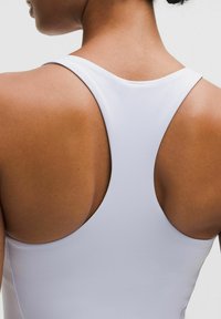 Vit atletisk linne med racerback-design, slät textur och låg halsringning, som framhäver hudtonen på bärarens rygg.