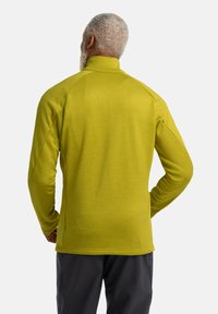 Langemanige pullover met hoge kraag in fel limoengroen stof, met raglanmouwen en een gladde textuur, gecombineerd met donkere broek.