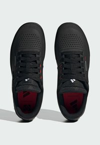 Scarpe sportive nere con tomaia testurizzata, chiusura con lacci, design perforato e accenti rossi; dotate di linguetta e soletta imbottite.