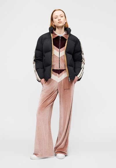 Μαύρο μπουφάν τύπου puffer με λευκές και μπεζ ρίγες, φορεμένο πάνω από βελούδινη φόρμα σε σχήμα ψαροκόκκαλου, μπορντό και ροζ, σε συνδυασμό με λευκά αθλητικά παπούτσια.