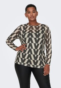 Maglietta a maniche lunghe con motivo zigzag in nero e beige, realizzata in un tessuto morbido, abbinata a pantaloni neri aderenti.