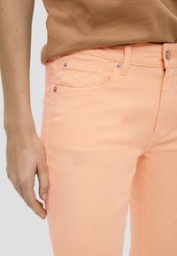 Perzikkleurige denimjeans met een aansluitend ontwerp, vijf-pocketstijl en subtiele stikseldetails. Zachte textuur met metalen hardwareaccenten.