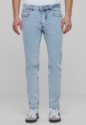 Vaaleansininen farkkukangas, slim fit -malli, jossa on klassinen viiden taskun muotoilu ja kontrastiväriset ompeleet. Yhdistetty valkoisiin urheilukenkiin.