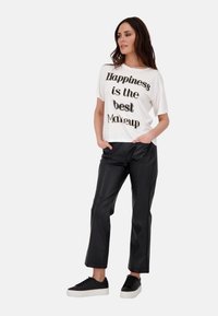 Weißes T-Shirt mit schwarzem Druck, kombiniert mit schwarzen Kunstlederhosen und schwarzen Sneakers mit einer weißen Sohle. Lässiges Outfit mit lockerer Passform.