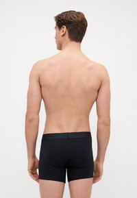 Svarta boxershorts med en slät textur, som har ett mjukt elastiskt midjeband. Modellen visas bakifrån, med bar hud synlig.