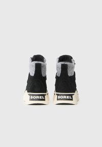 Svart suede høyhælte joggesko med grå ulldetaljer, kremfargede gummisåler og "SOREL" merkevare på hælen. Teksturert overflate, sporty design.