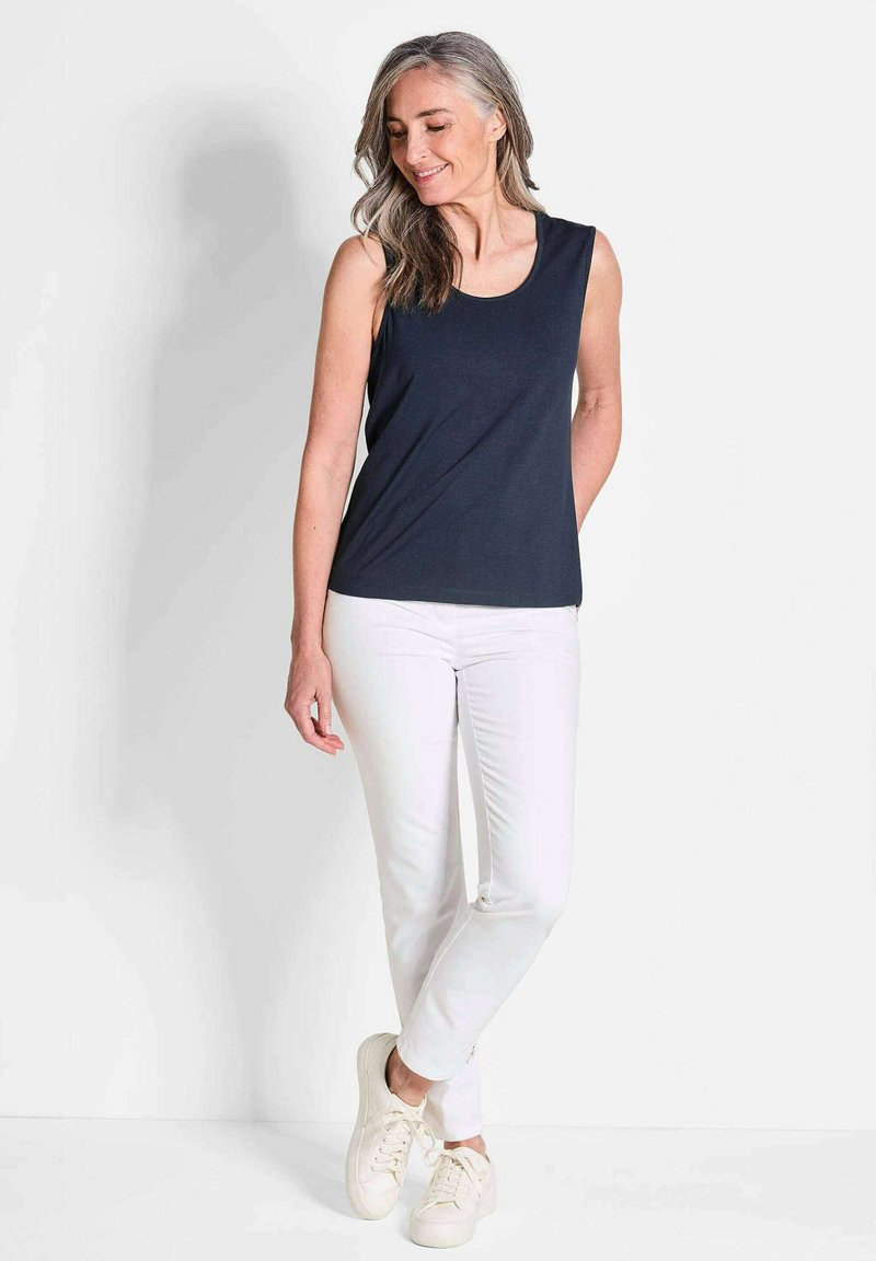 Marinefarbener ärmelloser Oberteil aus weichem Stoff mit Rundhalsausschnitt, kombiniert mit weißen Slim-Fit-Hosen und hellfarbigen Sneakers.