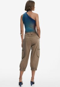 Bodycon cu un umăr, de culoare albastru gradient, asortat cu pantaloni cargo bej cu manșete elastice și buzunare mari pe laterale, purtat cu pantofi cu toc albaștri.
