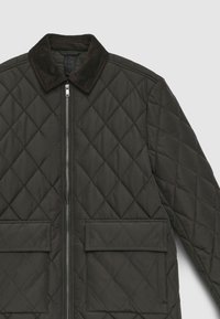 Steppjacke in Dunkelgrün mit Cordkragen, Reißverschluss vorne und zwei aufgesetzten Taschen. Mit Rautenmuster und strukturierter Oberfläche.