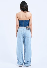 Jeansowy crop top z zapięciem na zamek, zestawiony z luźnymi, jasnoniebieskimi dżinsami, które mają widoczną metkę w pasie i dwie tylne kieszenie.