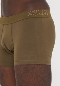 Olive green boxer briefs made of soft fabric, featuring a wide elastic waistband with the letters "SLG" printed on it. Smooth texture.