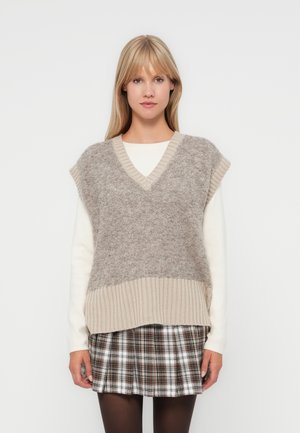 V-neck sleeveless vest in gray and beige knit with a textured finish, paired with a white long-sleeve shirt and plaid skirt.