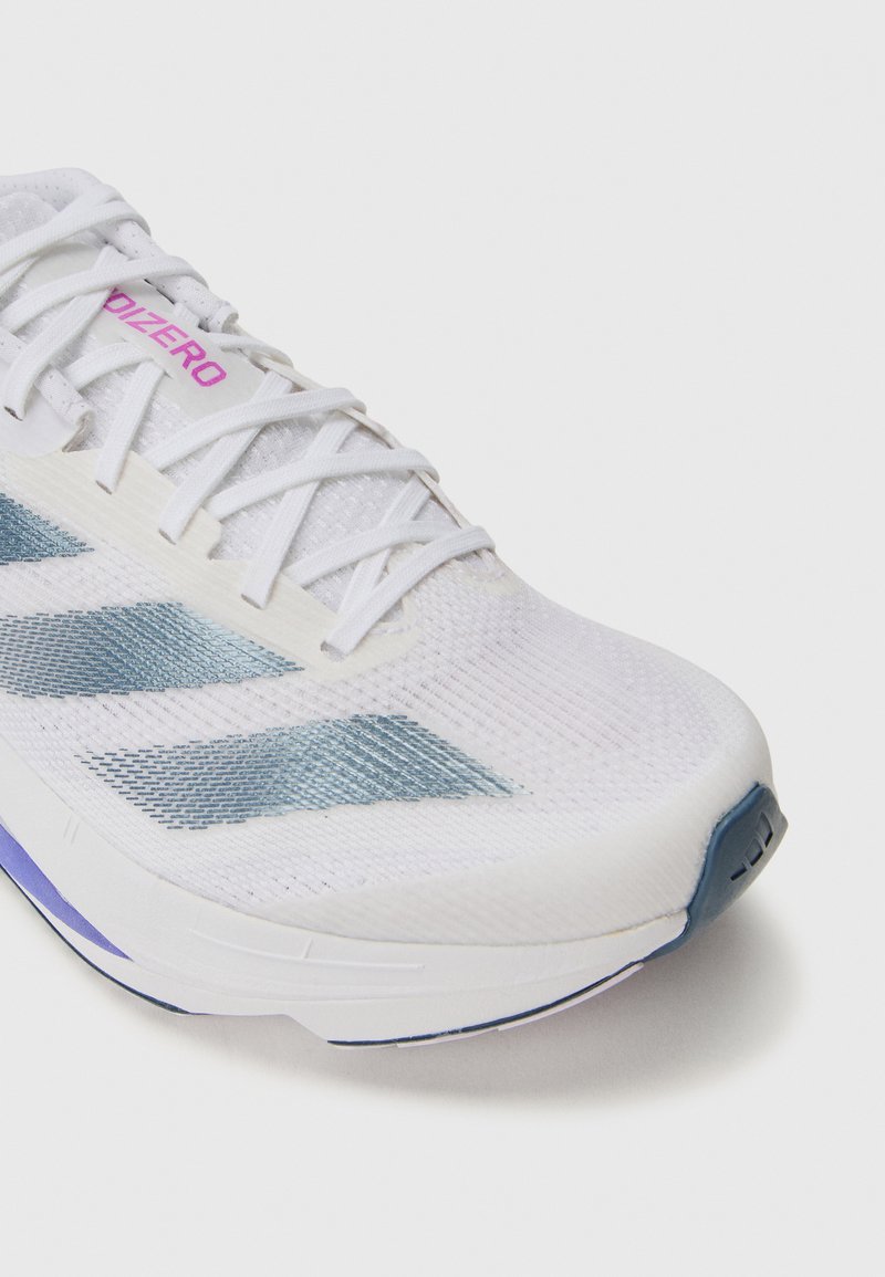 Zapatilla deportiva blanca con parte superior de malla, acentos azules y marcas en rosa. Presenta un diseño aerodinámico y un cuello acolchado para mayor comodidad.