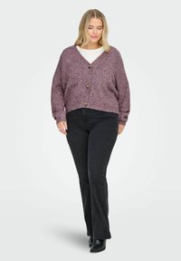 Übergroßer, tief mauvefarbener Cardigan aus strukturiertem Strick, mit einem V-Ausschnitt und drei dekorativen Knöpfen, kombiniert mit schwarzen Schlagjeans.
