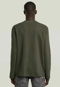 Chemise à manches longues en tissu olive texturé, avec un col rond, coupe décontractée et ourlet droit, vue de dos.