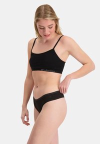 Mustat bambuista valmistetut crop top -paita ohuilla olkaimilla ja samaa materiaalia olevat mustat bambuistukkaat. Sujuva pinta, hengittävä kangas, minimalistikko muotoilu ja logotarkkuus.