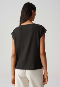 Zwarte, gestructureerde top met kapmouwen, met een ontspannen pasvorm en een rechte zoom, gecombineerd met lichtgekleurde broek.