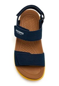 Sandalia azul marino con dos correas de Velcro ajustables, plantilla acolchada en color marrón y suela exterior de goma amarilla texturizada. El logo en la correa dice "Gioseppo."