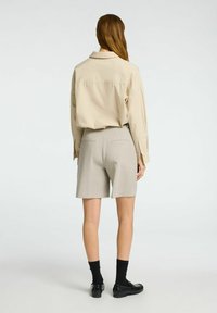 Beige langærmet skjorte, lysegrå skræddersyede shorts, sorte strømper og loafers. Skjorten har krave og en afslappet pasform. Shortsene har baglommer.