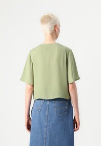 Kortermet, avkortet bluse i lysegrønn stoff, paret med et høyhudet denimskjørt med lommer og rekkeformet design.