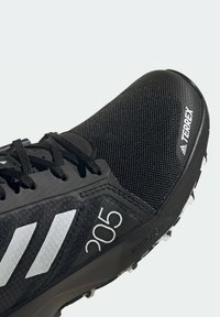 Scarpa sportiva nera con upper in rete, dettagli bianchi, caratterizzata dal logo a tre strisce, numero di modello 205 e suola testurizzata per una presa migliore.
