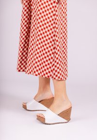 White wedge sandals with cork detail and open toe, paired with a red and white checkered skirt. Smooth texture and simple design.