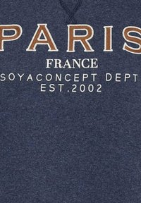 Marineblauwe stof met geborduurde tekst: "PARIS" in crème en bruin, "FRANKRIJK," "SOYACONCEPT DEPT," en "EST. 2002" in wit.