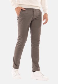 Pantaloni grigi slim-fit realizzati in tessuto misto cotone, con tasche laterali e una texture morbida. Abbinati a sneakers bianche.