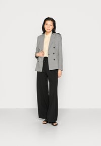 Blazer duplo em preto e branco com padrão xadrez, camisa bege e calças largas pretas. Tecido suave com um brilho subtil, design minimalista.