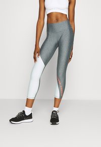 Szare i jasnoniebieskie obcisłe legginsy o gładkiej fakturze; posiadają pomarańczowe logo "Under Armour" na łydce oraz wysoki stan.