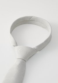 Cravate grise avec un motif géométrique discret, tissu texturé, et un design classique présentant une extrémité étroite et un nœud plié.