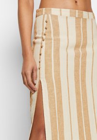 Randig linne kjol i kräm och tan med en sidoklyfta och dekorativa knappar längs sömmen. Slät textur med en avslappnad passform.