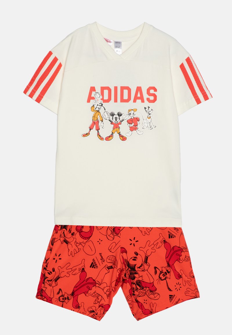 T-shirt crema con testo rosso "ADIDAS" e grafica di un personaggio; pantaloni corti rossi con stampa di personaggi dei cartoni animati. Mix di cotone, maniche corte e scollo a v.