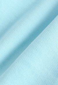 Tessuto blu chiaro con una consistenza morbida e liscia, caratterizzato da un delicato motivo a maglia e un'equa distribuzione del colore, che si drappeggia dolcemente.