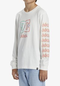 Langärmliges weißes T-Shirt aus Baumwolle mit mehrfarbigen Grafiken auf der Brust und orangefarbenem Text entlang des Ärmels. Klassischer Schnitt.