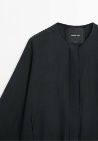 Czarna kurtka z długim rękawem, okrągłym dekoltem i ukrytym przednim zapięciem, z metką Massimo Dutti na wewnętrznym kołnierzu.