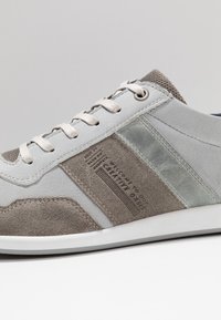 Jasnoszare sneakersy wykonane z zamszu i skóry, o smukłej sylwetce, z beżowymi akcentami i teksturowaną boczną panelf ze szczegółowym logo.