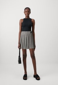 Top nero senza maniche abbinato a una gonna plissettata a scacchi bianca e nera. Scarpe nere senza lacci e una piccola borsa completano il look.