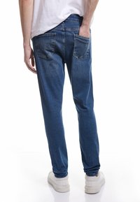 Jeans de mezclilla en azul medio con un corte recto. Incluye dos bolsillos traseros y una cinturilla, combinados con zapatillas blancas.