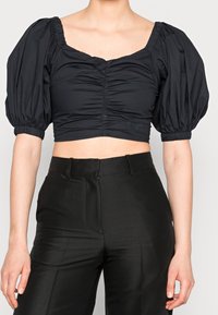 Blusa negra cortada con mangas abullonadas, que presenta un escote cuadrado y textura fruncida en la parte delantera. Combinada con pantalones negros de cintura alta.