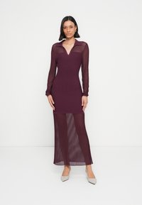 Lang burgunderrød kjole i gjennomsiktig ribbestrikket stoff, med krage, lange ermer og en tettsittende silhuett, med en splitt midt på leggen.