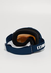 Óculos de esqui com uma armação azul-escura, lentes alaranjadas, espuma preta acolchoada e uma faixa de tecido ajustável com um logotipo branco.