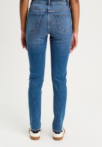 Niebieskie dżinsy z wysokim stanem, wąskim kroju, dwoma tylnymi kieszeniami oraz jasnym praniu. W połączeniu z białymi i czarnymi sneakerami z brązową podeszwą.