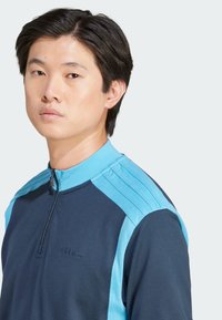 Jūras spēku zip-up sporta krekls ar gaiši ziliem akcentiem, ribota tekstūra un trīs svītras uz pleciem. Priekšpusē ir logotips.