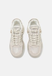 Beżowe buty sportowe z siateczkowymi i zamszowymi materiałami, okrągłe noski, sznurowadła oraz teksturowana podeszwa z widoczną wkładką powietrzną.