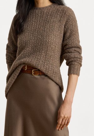 Femme portant un pull en maille marron texturé, rentré dans une jupe marron soyeuse avec une ceinture beige à boucle dorée.