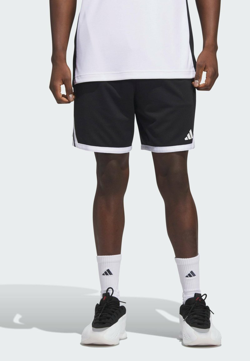 Pantalones cortos deportivos negros con acentos blancos y tres rayas, combinados con calcetines blancos y zapatillas negras. Diseñados para la comodidad y el movimiento.